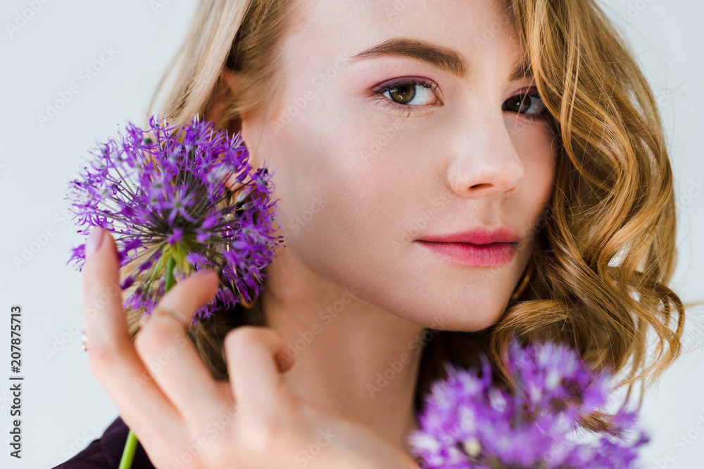 beautiful girl holding fresh violet flowers and looking at camera isolated on grey beautiful girl holding fresh violet flowers and looking at camera isolated on grey