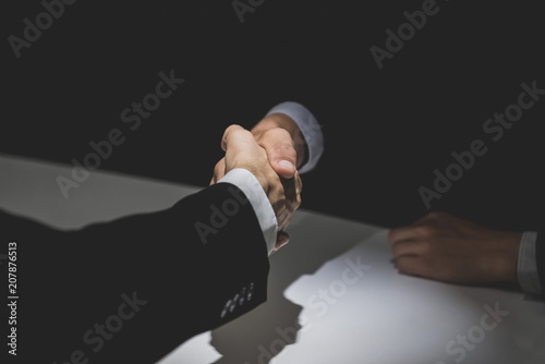 Business partners making handshake in dark shadow