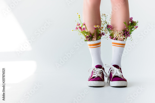 cropped shot of girl with fresh flowers in socks on grey