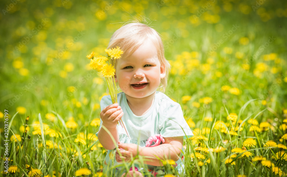 Beautiful happy little baby girl sitting on a green meadow with yellow flowers dandelions Beautiful happy little baby girl sitting on a green meadow with yellow flowers dandelions