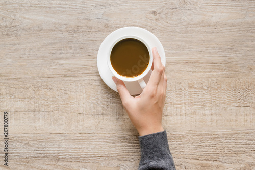 Female hand holding cup of coffee on wood texture background.