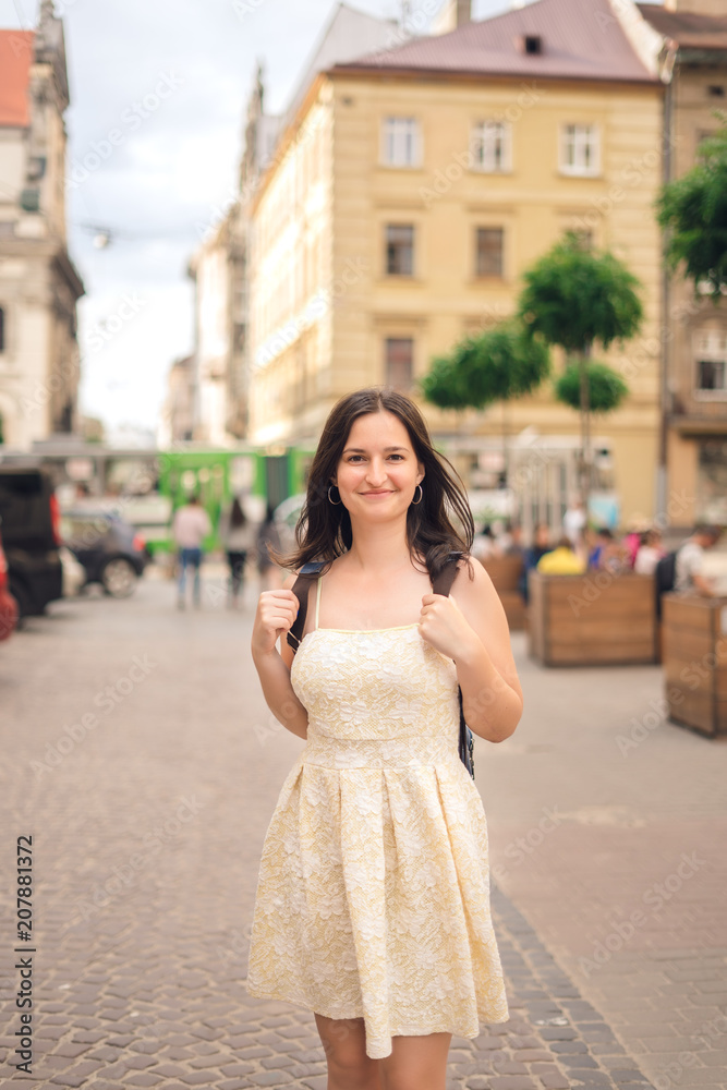 Brunette girl in dress and backpack in city. Girl in yellow summer dress