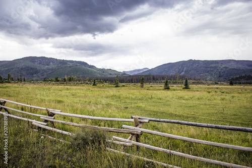 Wood Fence Runs along a Meadow with the Rocky Mountains and Grey Clouds in the Distance, Colorado, USA