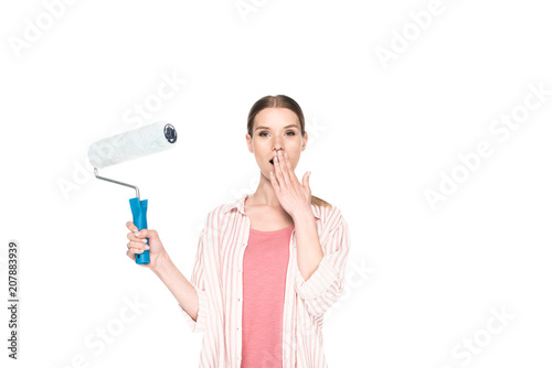 young woman closing mouth by palm and holding paint roller isolated on white background