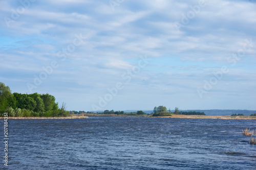 A river on a sunny summer day with trees on the shore and a beautiful sky in the clouds.