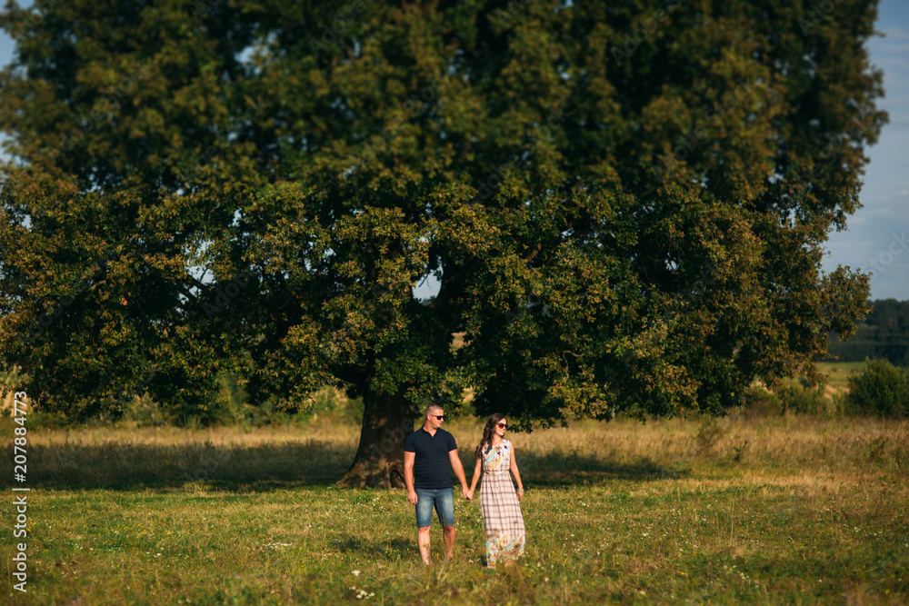 Handsome guy and an attractive girl hug each other near a large green tree. Love story Handsome guy and an attractive girl hug each other near a large green tree. Love story