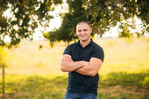 Attractive guy stand near a large green tree. Love story