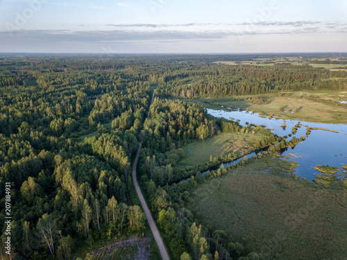 drone image. country lake surrounded by pine forest and fields from above © Martins Vanags