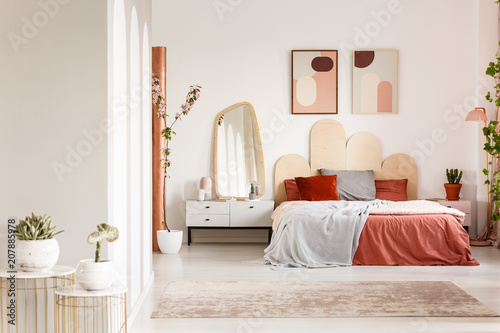 Mirror on white cabinet next to orange bed under posters in modern bedroom interior. Real photo