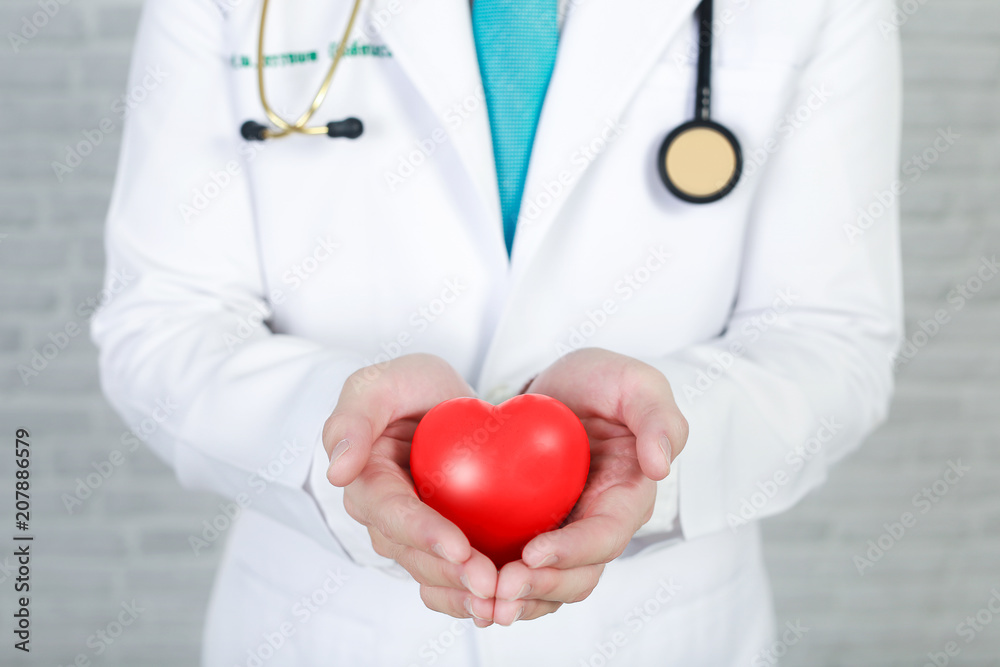 Young man doctor holding a red heart, standing on wall background. Young man doctor holding a red heart, standing on wall background.