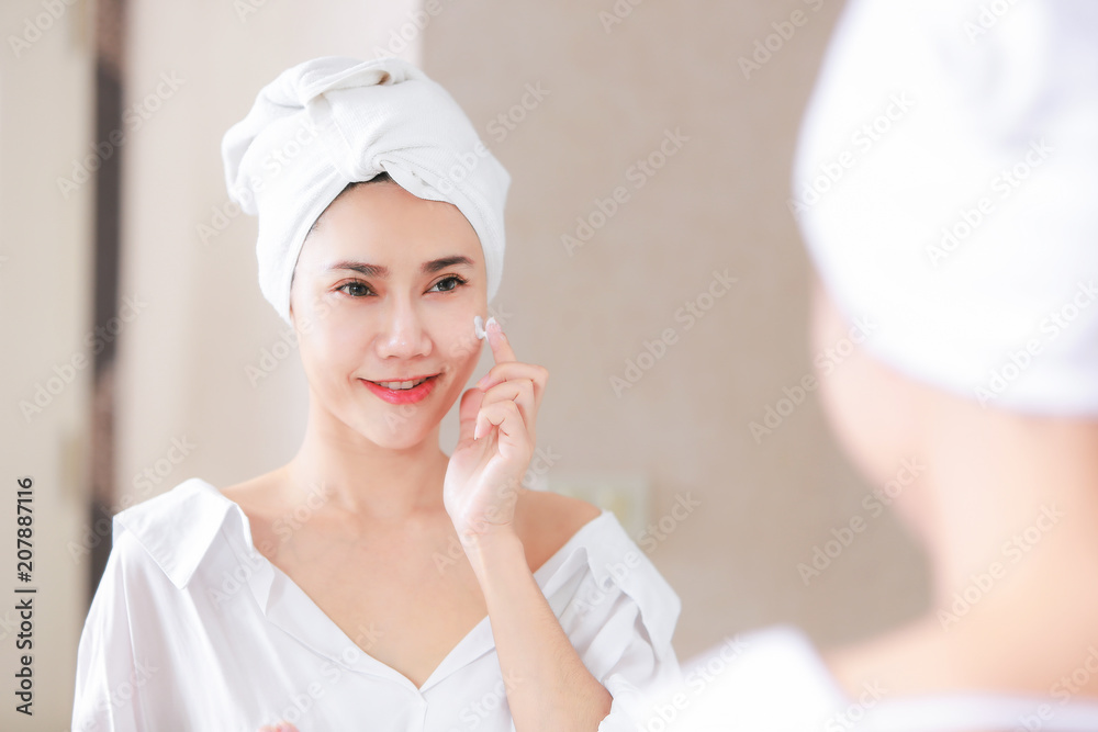 Young asia woman applying foundation or moisturizer on her face in front of mirror. Young asia woman applying foundation or moisturizer on her face in front of mirror.