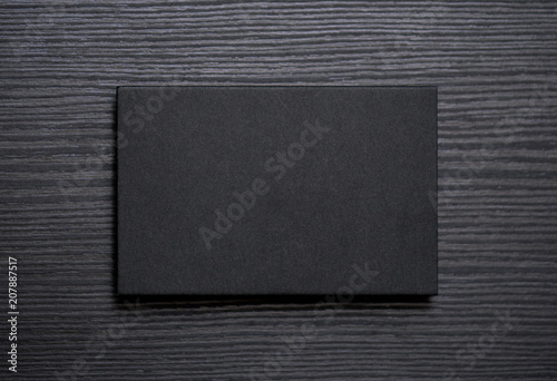 Mockup of blank textured black business card on dark wood background