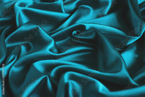 Close up of ripples in turquoise silk fabric. Satin textile background.