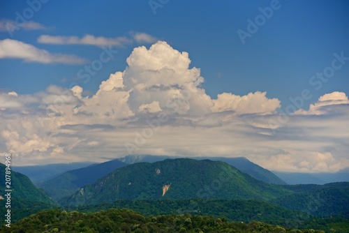 A beautiful large cloud on a green forested mountain. Summer mountain landscape.