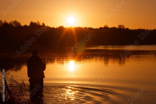 Silhouette of a fisherman during sunrise on lake