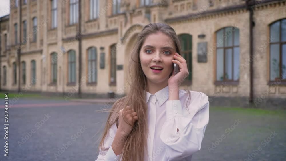 Young beautiful happy girl answers call during going from university in daytime in summer, communication conception