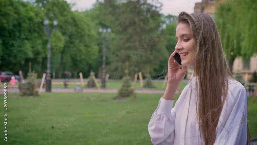 Young beautiful happy girl is talking on phone and going in park in daytime in summer, communication conception Young beautiful happy girl is talking on phone and going in park in daytime in summer, communication conception
