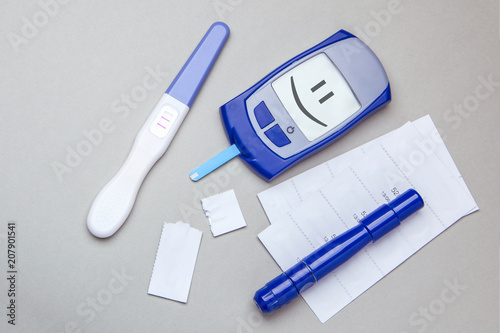 Diabetes mellitus, increased blood sugar in pregnant women. Glucometer and positive test for variability. Smiling face on display. Gray background