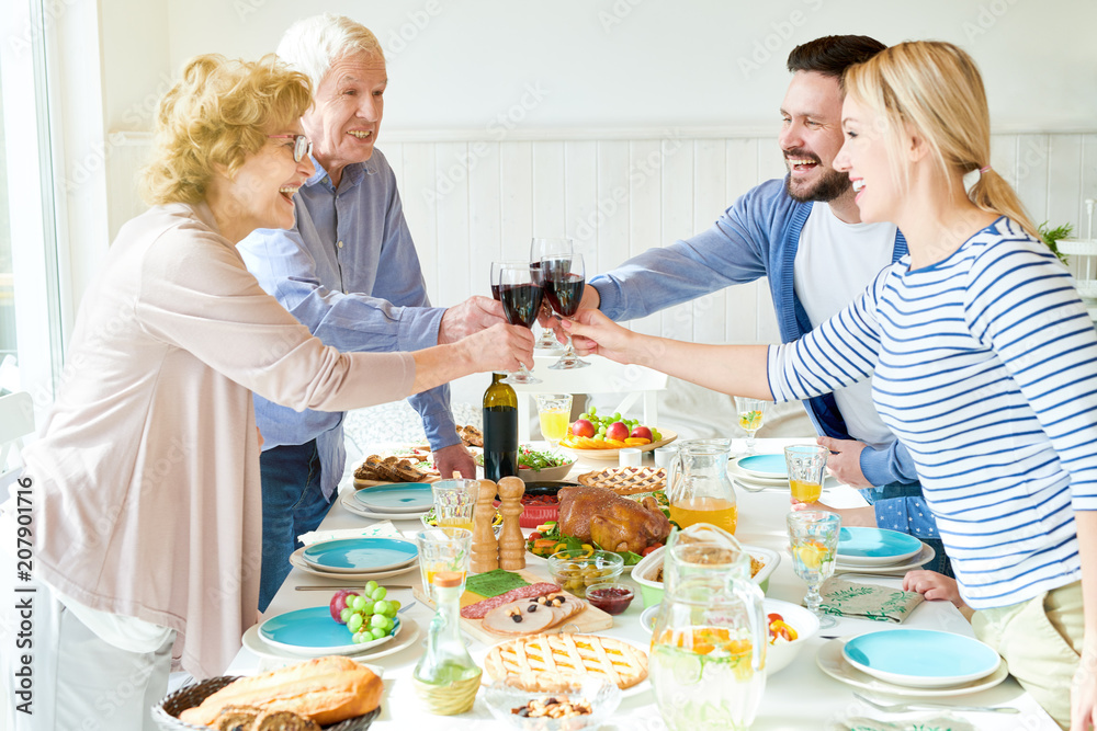 Side view portrait of happy two generation family enjoying dinner together clinking glasses at festive table with delicious dishes and smiling during holiday celebration, copy space