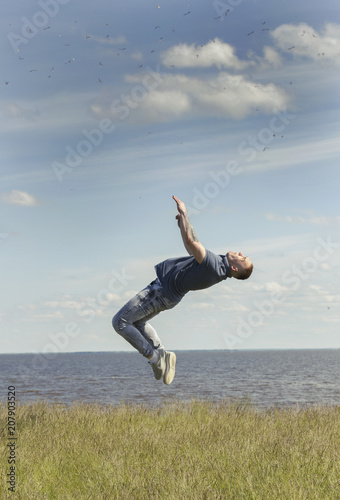 Young man performing flips on the hill over the river at summer sunny day