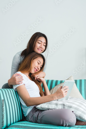 Beautiful young asian women LGBT lesbian happy couple sitting on sofa buying online using tablet in living room at home. LGBT lesbian couple together indoors concept. Spending nice time at home.