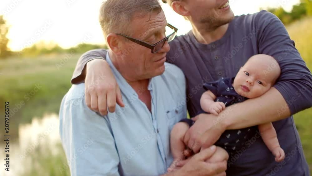 Three generations of one family embrace. Men rest on the river bank. Grandpa, son and grandson spend time together. Happy family vacation