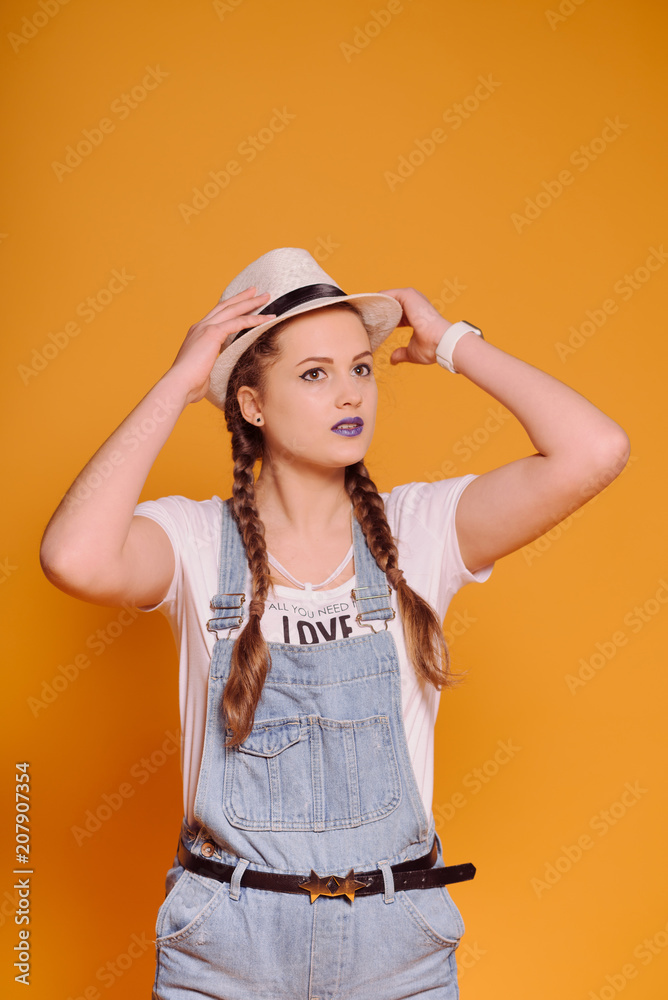 Happy Student Girl. Summer urban style.Attractive girl in summer clothes holding hat, looking away and smiling, against yellow background Happy Student Girl. Summer urban style.Attractive girl in summer clothes holding hat, looking away and smiling, against yellow background