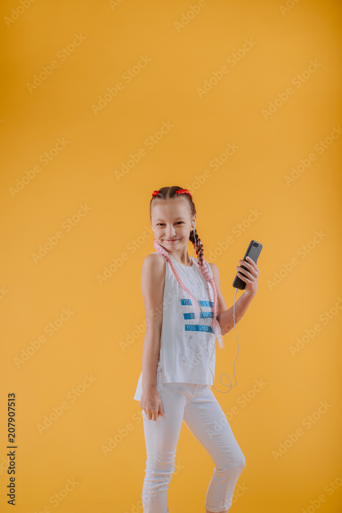 Smiling girl enjoying favorite song and dancing in white tank-top. portrait of excited curly teen having fun in headphones with phone.Stylish teenage girl is enjoying her modern kanekalon hair Smiling girl enjoying favorite song and dancing in white tank-top. portrait of excited curly teen having fun in headphones with phone.Stylish teenage girl is enjoying her modern kanekalon hair