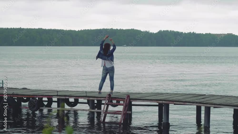 Young woman jumps on old pier and turns around and looks at camera smiling Young woman jumps on old pier and turns around and looks at camera smiling