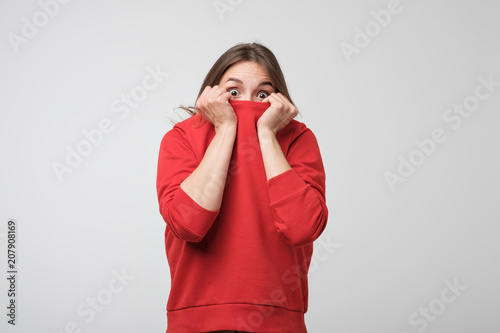 A girl with a social phobia hides her face in a sweater. She looks frightened at the camera