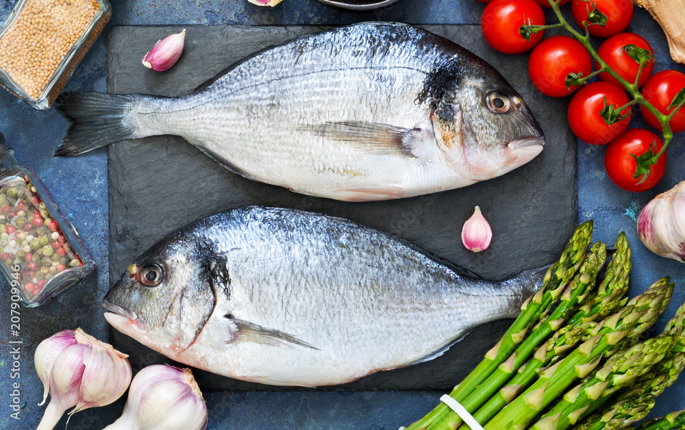 Fresh, raw Dorado fish with asparagus, tomatoes and spices on a concrete background. Ingredients for cooking. Fresh, raw Dorado fish with asparagus, tomatoes and spices on a concrete background. Ingredients for cooking.