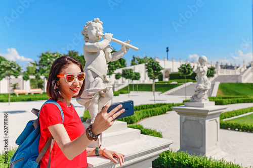 Photography Young female traveler making selfie with smart phone with Cupid statue in summer