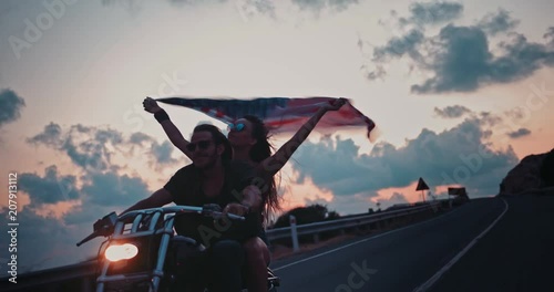 Young motorcyclist couple riding on motorbike and waving American flag