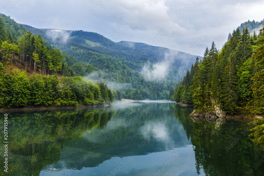 Fototapeta premium Landscape with lake and misty forest in mountains in a rainy day