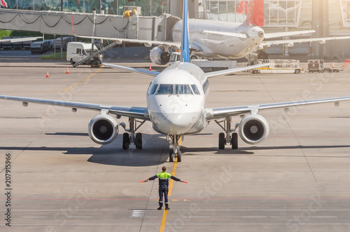 Aviation marshall supervisor meets passenger airplane at the airport. Aircraft is taxiing to the parking place. Ground Crew in the signal vest. photo