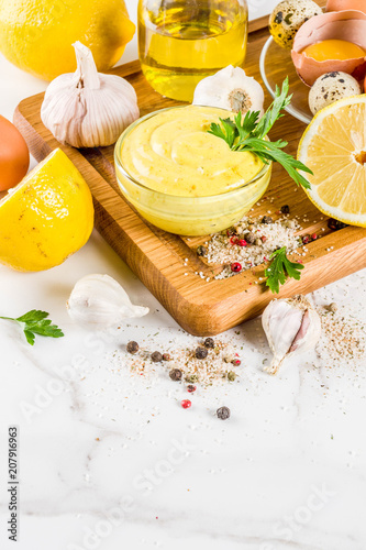 Homemade mayonnaise sauce with ingredients - lemon, eggs, olive oil, spices and herbs, white marble kitchen table copy space