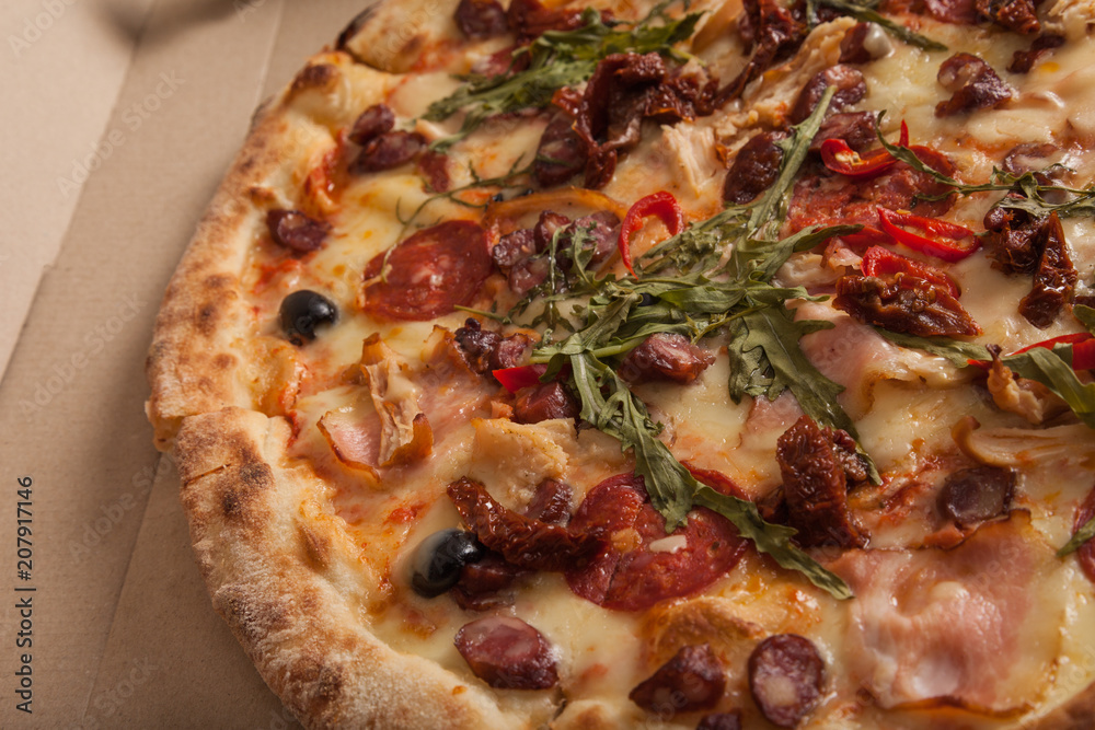 Delicious crispy Italian pizza on craft paper cardboard. Closeup of Pizza with salami, sausages, olives, hot red chili peppers, ham and sun-dried tomatoes. Restaurant menu, Italian food. Delivery Delicious crispy Italian pizza on craft paper cardboard. Closeup of Pizza with salami, sausages, olives, hot red chili peppers, ham and sun-dried tomatoes. Restaurant menu, Italian food. Delivery