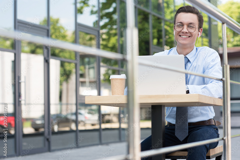 handsome smiling young freelancer in eyeglasses using laptop outside modern building handsome smiling young freelancer in eyeglasses using laptop outside modern building