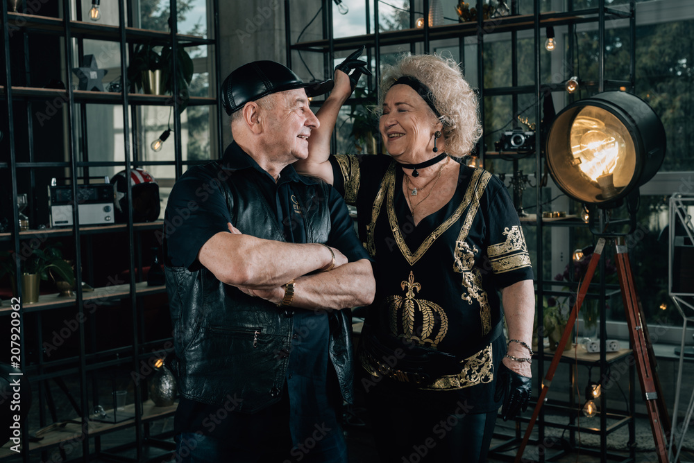 Happy couple of retirees in biker clothes.Senior motorcyclist with a black helmet and goggles looking at the camera.Unusual retired couple.Biker grandmother and biker grandfather. Biker couple.