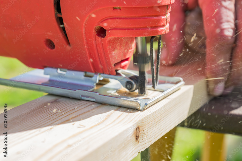 wood worker cutting wooden panel with jig saw outdoors, Close-up view of men working with electric jigsaw and wooden plank.