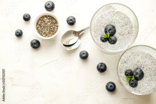 Two portions of chia pudding with vegan almond milk, blueberry & seeds on the side, served in glasses. Healthy vegetarian breakfast, berries & greek yogurt, spoon. Background, copy space, close up.