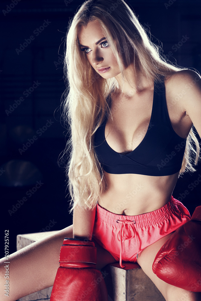 Half portrait of young blonde woman with long hair, dressed in black sports  bra, pink shorts