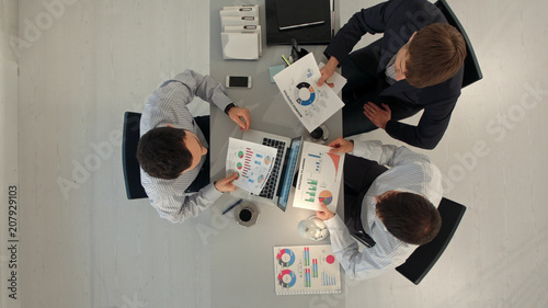 Creative team displaying charts  with laptop and tablet pc computers sitting at table in office. Top view