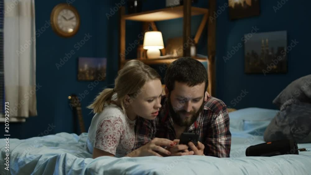 Young girl with smartphone and lying on bed in night and surfing Internet together having fun and relaxing Young girl with smartphone and lying on bed in night and surfing Internet together having fun and relaxing