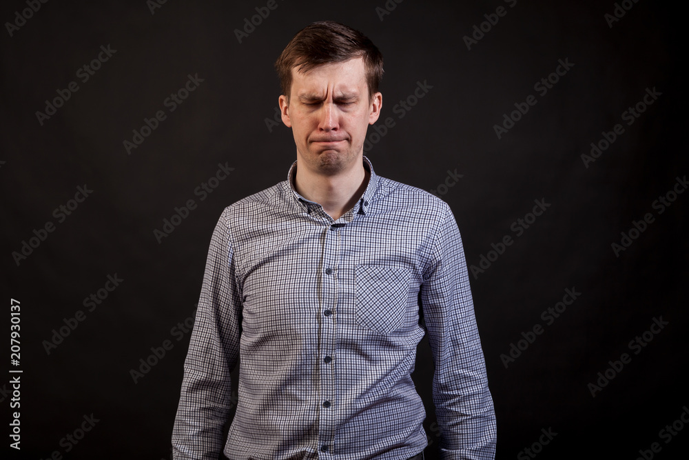 A dark haired white man with a sad and boring face closed eyes in a plaid shirt and jeans on a black isolated background