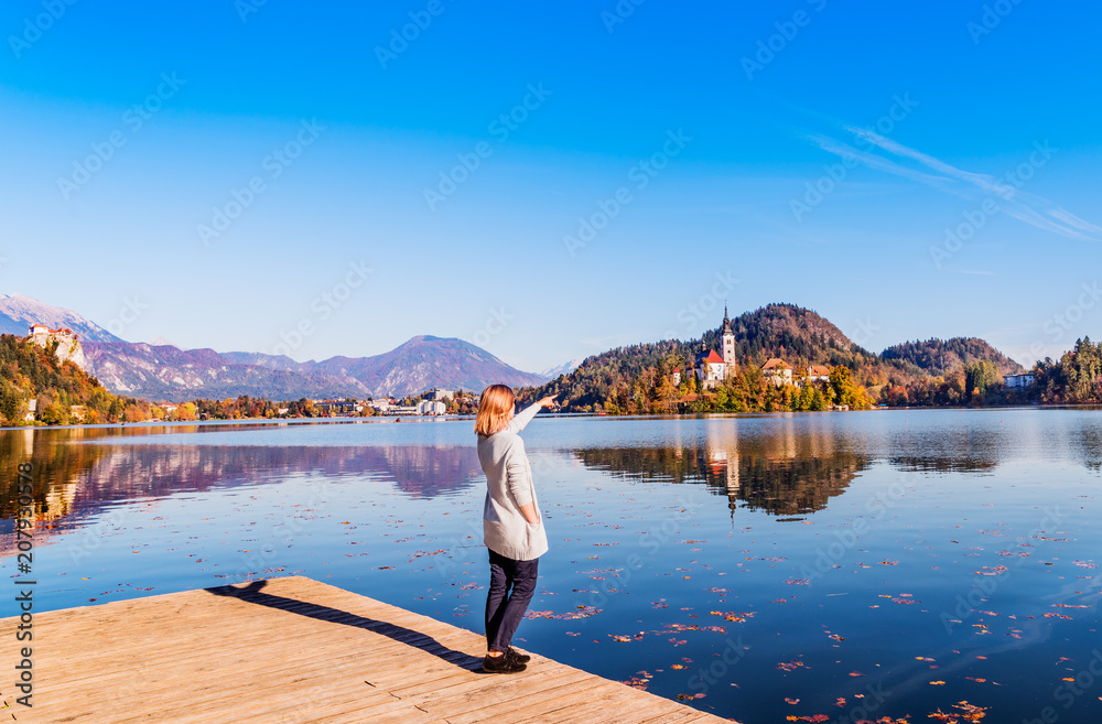 Naklejka premium Travel Slovenia, Europe. Young woman looking at Bled Lake and Alps Mountain. Bled Lake is amazing tourist attractions. 