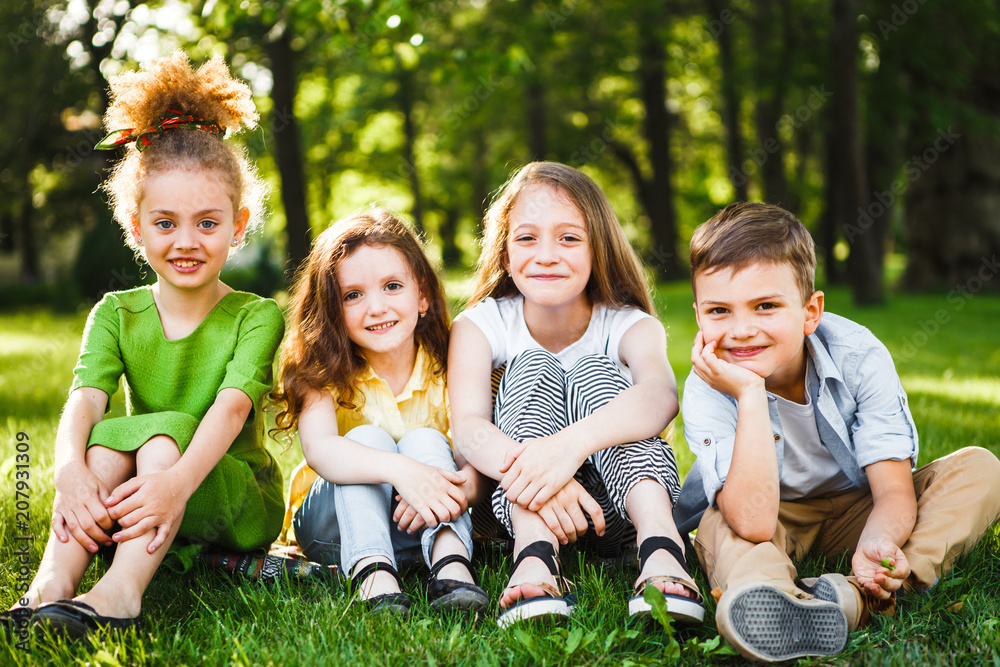 Fototapeta premium A group of children of school and preschool age are sitting on the green grass in the park.