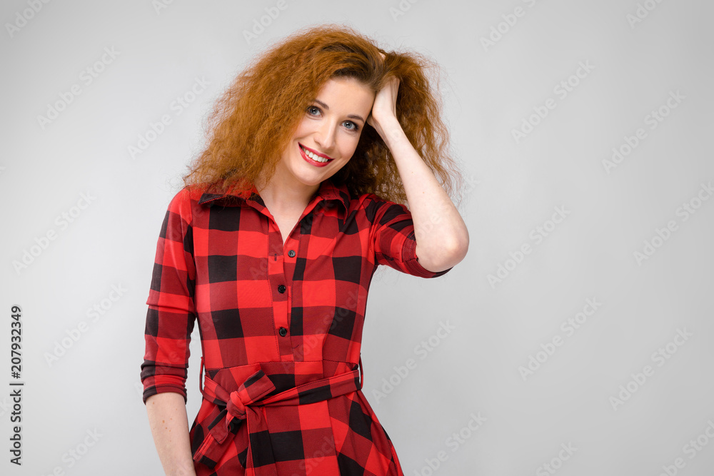Portrait of beautiful redhead happy young woman smiling holding her hand on hair on gray background Portrait of beautiful redhead happy young woman smiling holding her hand on hair on gray background