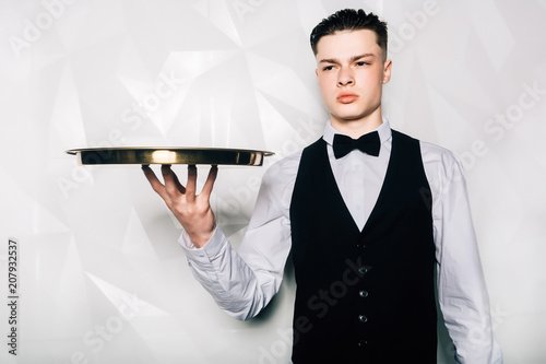 Portrait of male waiter who is holding tray in hall of restaurant.Portrait of waiter with serving tray meeting restaurant guests