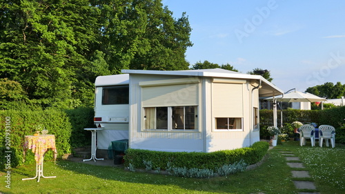 Caravan mit einer festen Veranda aus Markisenstoff, Glasschiebefenster und Rollläden auf einem deutschen Campingplatz. Komfortabel und gut gepflegt.